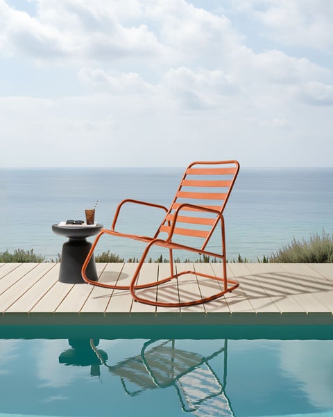 Szene mit einem orangefarbenen Liegestuhl, einem Beistelltisch, Getränken und einer Sonnenbrille am Pool