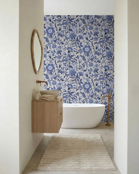 Modernes Badezimmer mit freistehender Badewanne, hölzernem Waschtisch mit Steinbecken und blau gemusterter Blumentapete an der Wand.