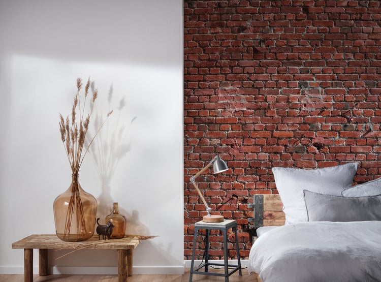 Tapete in Backsteinoptik an einer Wand in einem modernen Schlafzimmer mit rustikalem Holztisch und Bett.