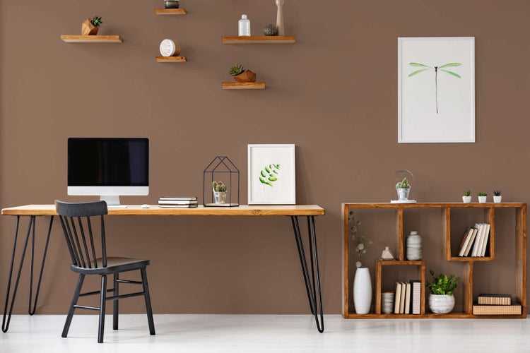 Moderner Arbeitsplatz mit Holzschreibtisch, schwarzem Stuhl und brauner Wandfarbe. Dekorative Wandregale und ein Holzregal sorgen für Ordnung.