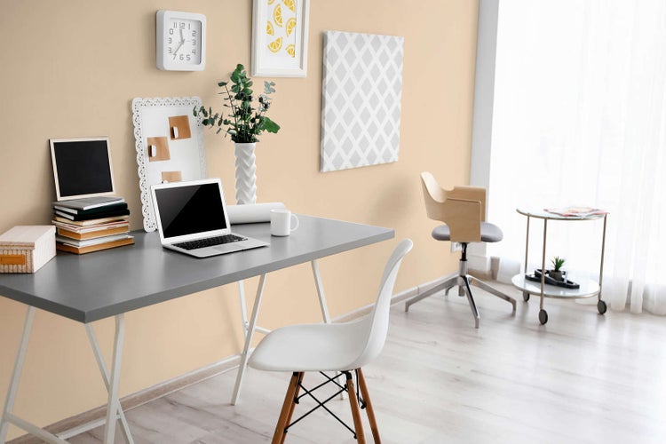 Modernes Homeoffice mit grauem Schreibtisch, weißem Stuhl und Wanddekoration in einem hellen, organisierten Raum.