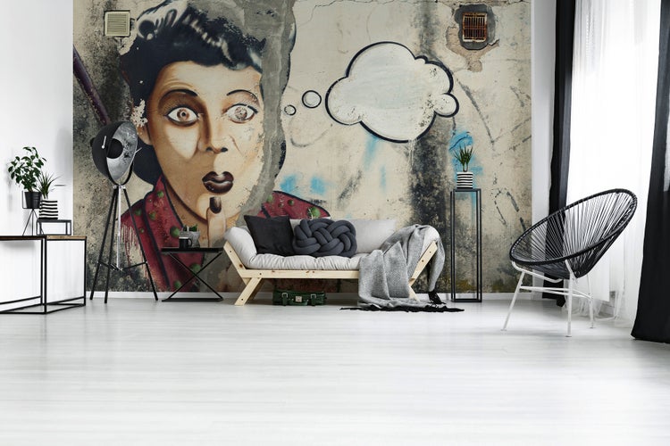 Modernes, helles Wohnzimmer mit Street-Art-Fototapete eines Frauengesichts, Holzsofa, Stativ-Stehlampe und Drahtstuhl.