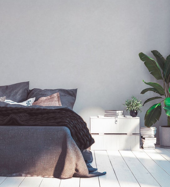 Schlafzimmer mit Bett, Nachttisch, Zimmerpflanzen und Bücherstapel