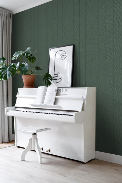 Wohnraum mit grüner Tapete mit Pfeilmuster, weißem Klavier, Hocker und Zimmerpflanze