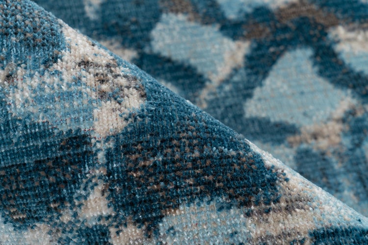 Nahaufnahme eines blau-grau gemusterten Teppichs mit abstraktem geometrischem Muster und Kurzflor.
