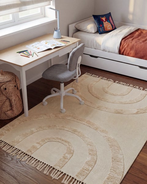 Kinderschlafzimmer mit Teppich mit Regenbogenmuster, Schreibtisch, Kinderstuhl, Bett und Korb in Form eines Elefanten.
