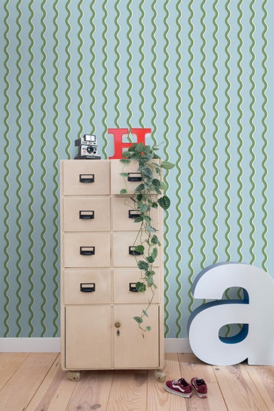 Zimmer mit Wellenmuster-Tapete, einem Apothekerschrank aus Holz, einer Hängepflanze und hellem Holzboden.