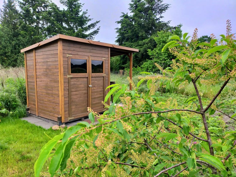 Holz-Gartenhaus mit Flachdach, Doppeltür inklusive Fenstern und seitlichem Schleppdach im Garten.