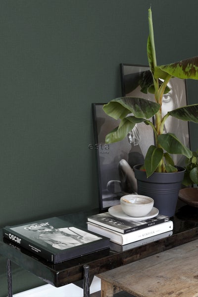 Nahaufnahme einer Wand mit grüner Textiltapete, dekoriert mit einem Tisch mit Pflanzen, Büchern und gerahmten Bildern.