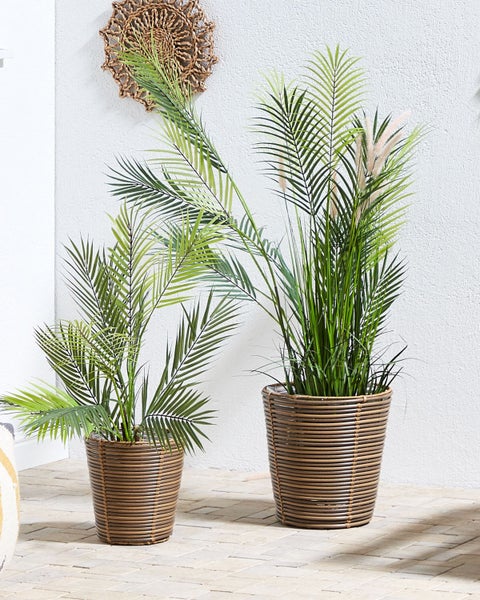 Zwei künstliche Pflanzen in braunen Rattan-Übertöpfen dekorieren einen Raum.