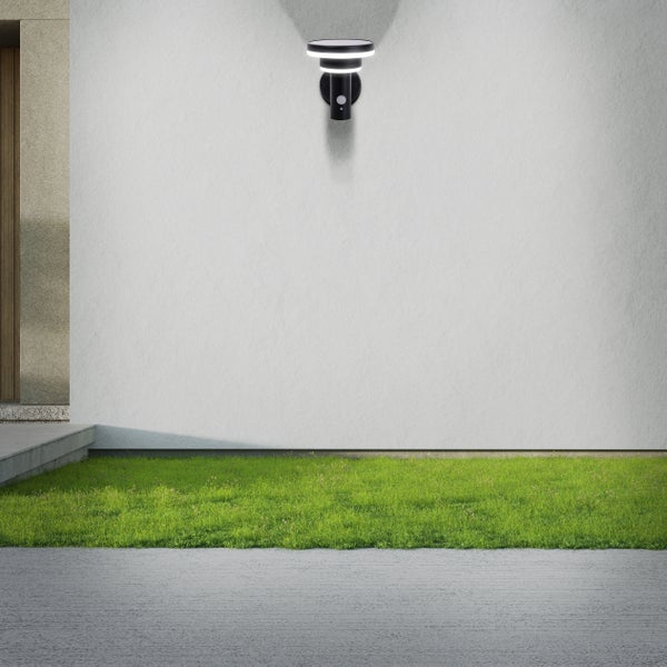 Außenwandleuchte mit Bewegungsmelder an einer Hauswand über einem Rasen