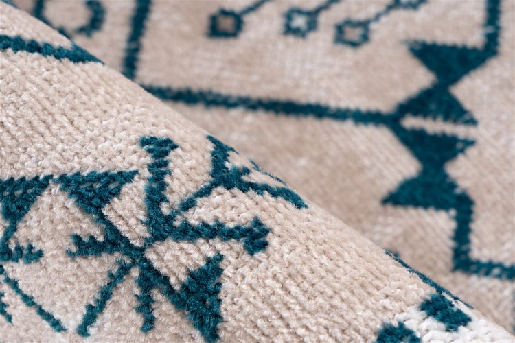 Detailaufnahme eines gewebten Teppichs mit blauem geometrischem Muster auf beigem Untergrund.