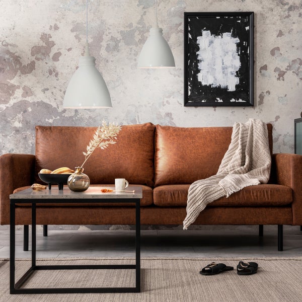 Wohnzimmer mit braunem Ledersofa, Couchtisch, zwei Pendelleuchten und Kunstwerk an der Wand.