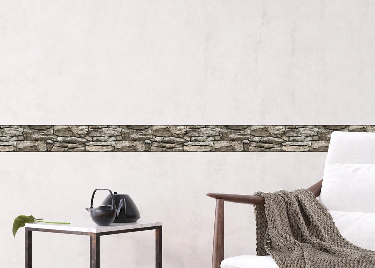 Tapetenbordüre in Steinoptik an einer Wand in einem modernen, hellen Wohnraum mit Beistelltisch und Sessel.