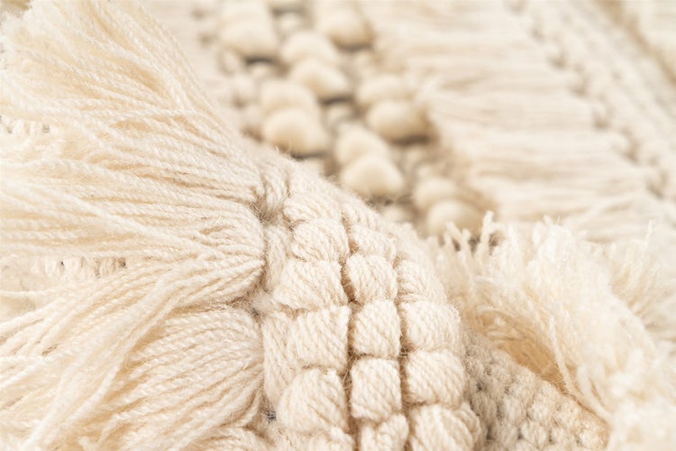 Detailaufnahme eines gewebten Teppichs mit Fransen und einer strukturierten Oberfläche aus dicken Knoten.