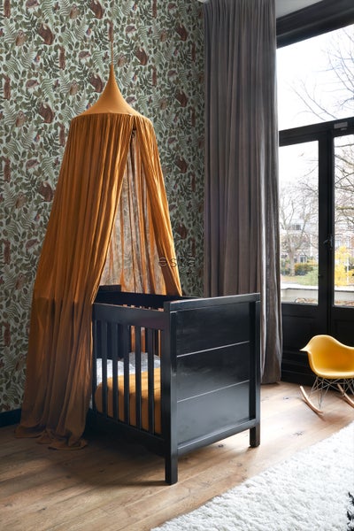 Kinderzimmer mit schwarzem Babybett unter einem Baldachin und einer Tapete mit Tiermotiven