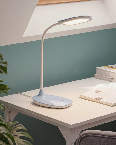 Moderne Schreibtischleuchte mit flexiblem Hals auf einem weißen Schreibtisch mit Büchern und einer Pflanze.