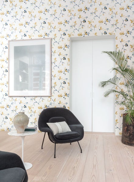 Wohnzimmer mit floral gemusterter Tapete, Sessel und Zimmerpflanze