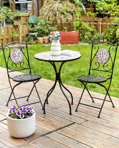 Gartenszene mit Mosaiktisch, zwei Mosaikstühlen und einem Blumentopf mit lila Blumen auf einer Holzterrasse