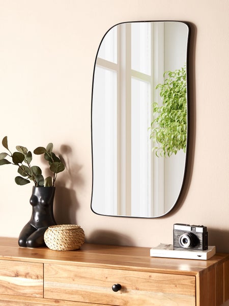 Asymmetrischer Spiegel mit schwarzem Rahmen auf einer Holzkommode