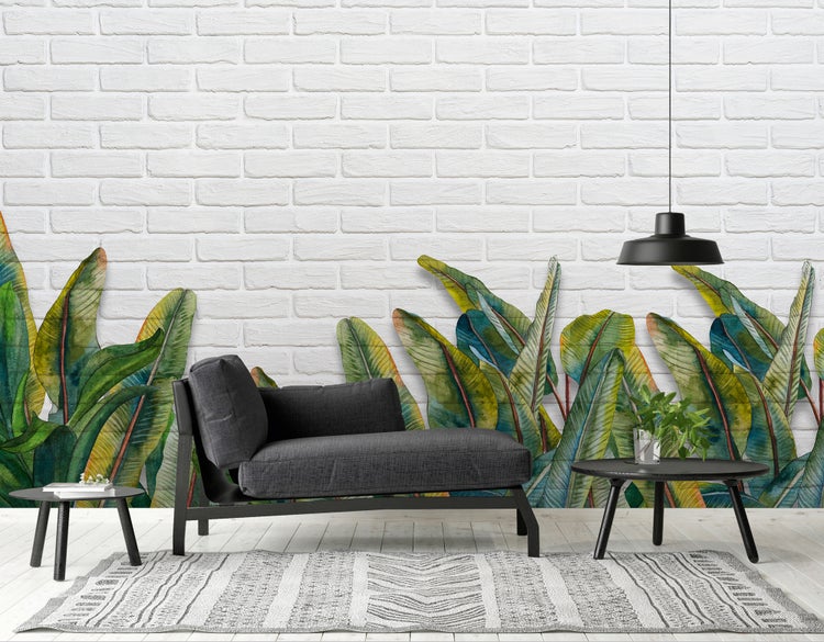 Modernes Wohnzimmer mit Fototapete in botanischem Design mit großen grünen Blättern vor weißer Ziegeloptik, davor eine dunkle Récamiere.