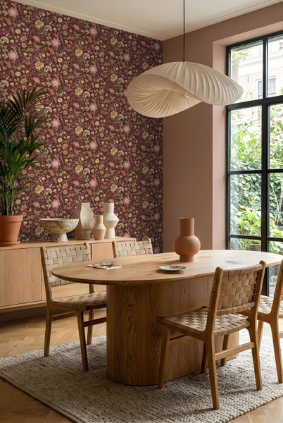 Modernes Esszimmer mit ovalem Holztisch, Geflechtstühlen, floraler Tapete und einer großen Wellen-Pendelleuchte.