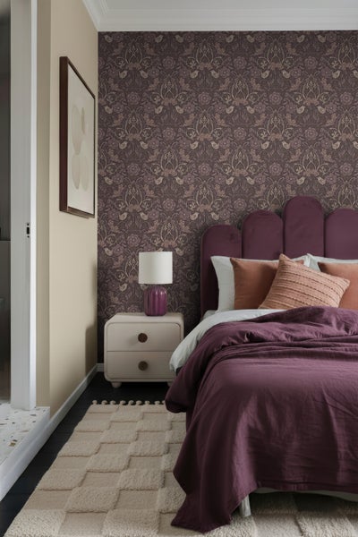 Schlafzimmer mit gemusterter Tapete, Bett, Nachttisch, Lampe und Teppich