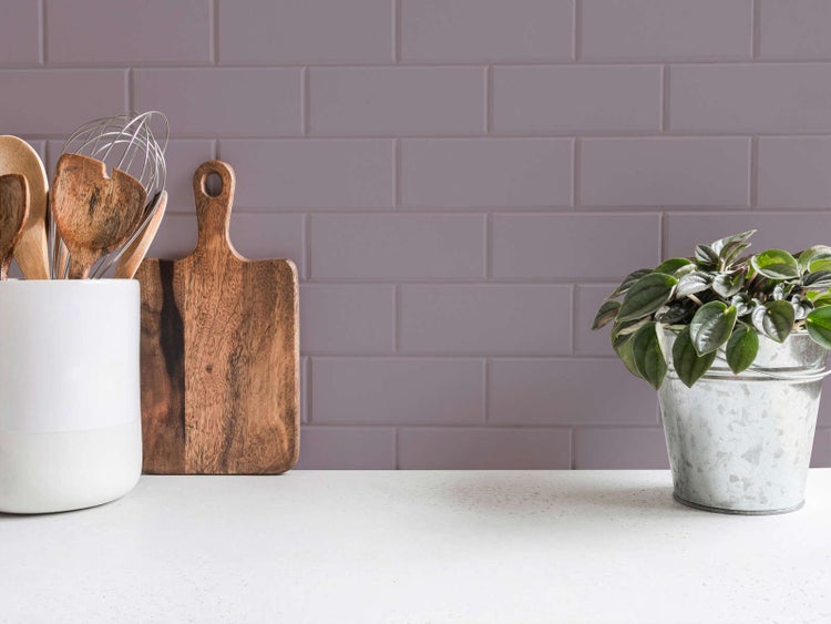 Helle Küche mit Wandfliesen in Metro-Optik, Schneidebrett aus Holz, Küchenutensilien und Zimmerpflanze auf der Arbeitsplatte.
