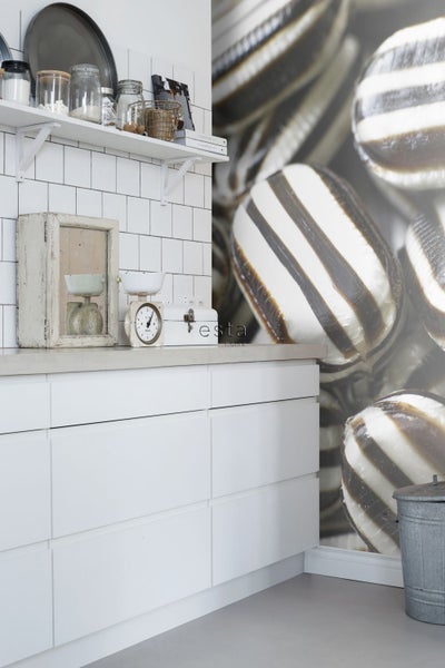 Küchenszene mit weißen Schränken, Waagen und Dekoration auf der Arbeitsplatte vor einer Wandtapete mit Süßigkeitenmuster.