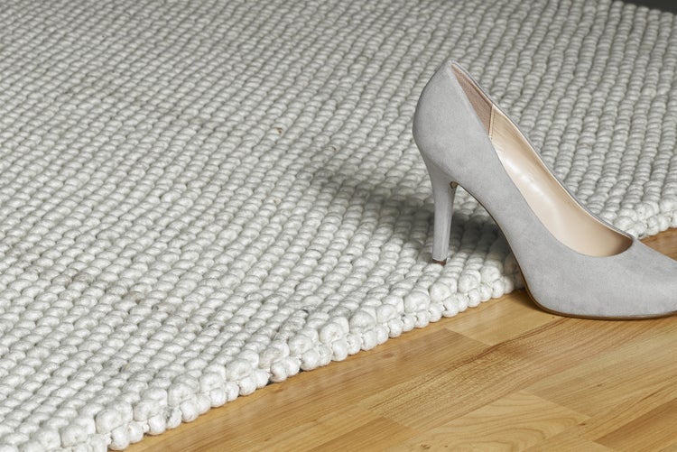 Strukturierter Teppich mit grober Schlingenstruktur auf einem Holzboden mit einem Pumps.