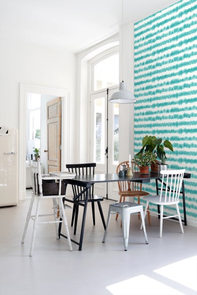 Heller Raum mit Esstisch und verschiedenen Stühlen vor einer Wand mit Streifenmuster