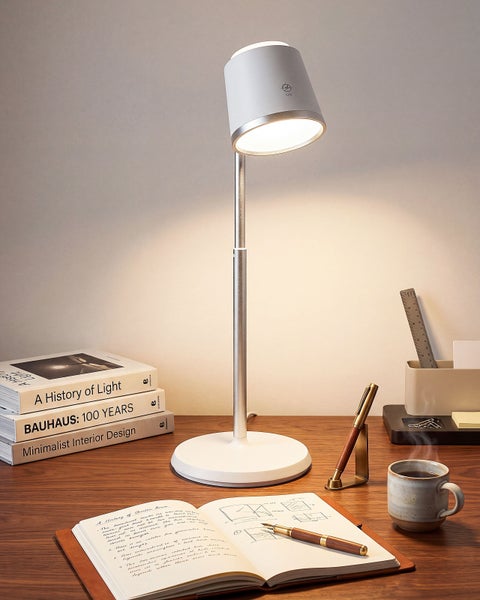 Moderne Schreibtischleuchte mit LED-Beleuchtung auf einem Holzschreibtisch mit Büroutensilien und Büchern.