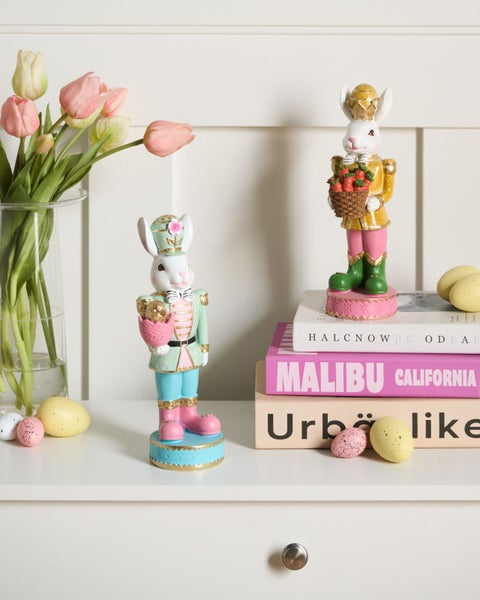 Zwei dekorative Osterhasen-Figuren im Nussknacker-Stil auf einem weißen Regal mit Tulpen und Ostereiern.