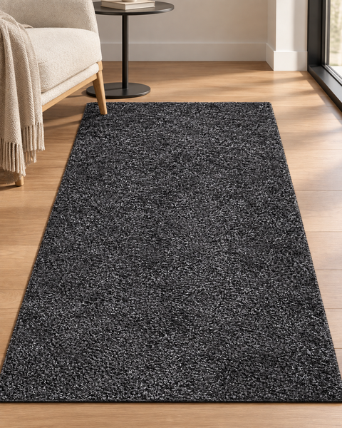 Ein moderner, rechteckiger Hochflor-Teppich in strukturierter Optik, der vor einem Sessel mit Beistelltisch auf einem hellen Holzboden liegt.