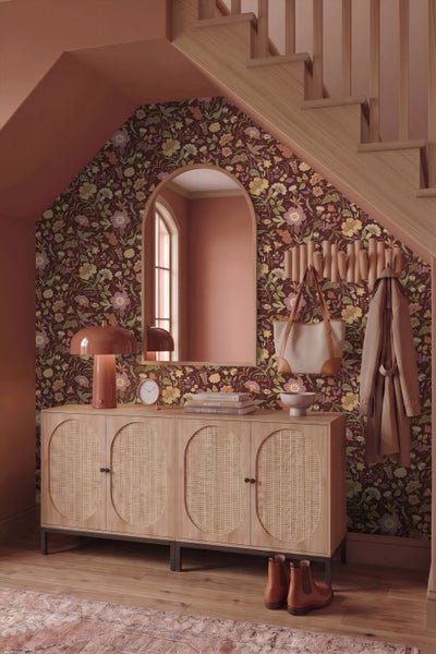 Eingangsbereich mit floraler Tapete, einem hölzernen Sideboard mit Rattan-Fronten, einem Rundbogenspiegel und einer Treppe aus hellem Holz.