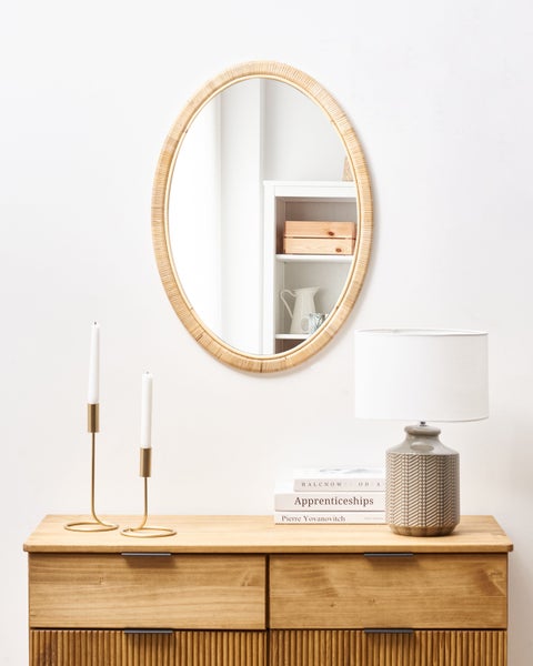 Dekoratives Interieur mit ovalem Spiegel, Tischleuchte, Kerzenständern und Holzkommode