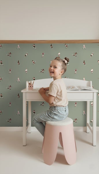 Kind sitzt an einem Schreibtisch vor einer grünen Tapete mit Fußballmotiven