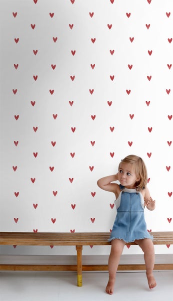 Mädchen sitzt vor einer weißen Wand mit Herzmuster auf einer Holzbank