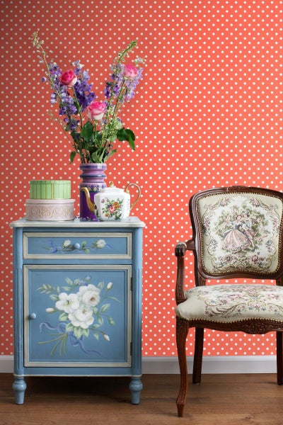Dekoratives Interieur mit Blumen, Kommode und Stuhl vor gepunkteter Wand