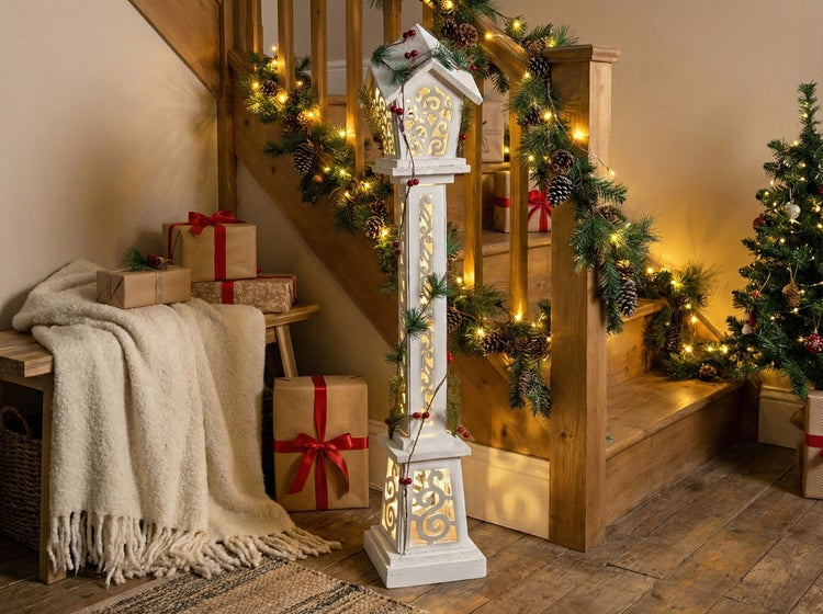 Weihnachtliche Dekoration mit beleuchtetem Deko-Leuchtturm, Tannengirlande, Geschenken und Weihnachtsbaum im Treppenhaus