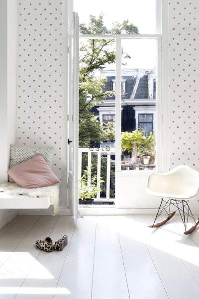 Heller Raum mit Tapete mit Herzmuster, Sitzgelegenheit und geöffneter Tür zum Balkon.
