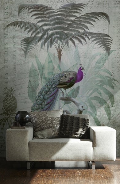 Fototapete mit Pfau, Palmwedeln und Vintage-Schriftzügen hinter einem Sessel im Wohnzimmer.