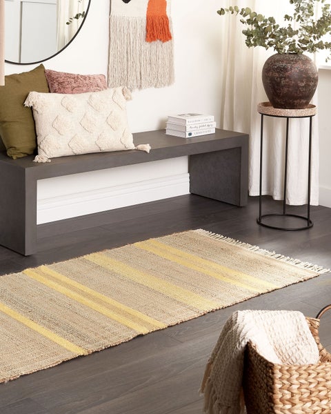 Moderner Eingangsbereich mit grauer Sitzbank, strukturierten Kissen und einem gestreiften Juteteppich auf dunklem Holzboden.