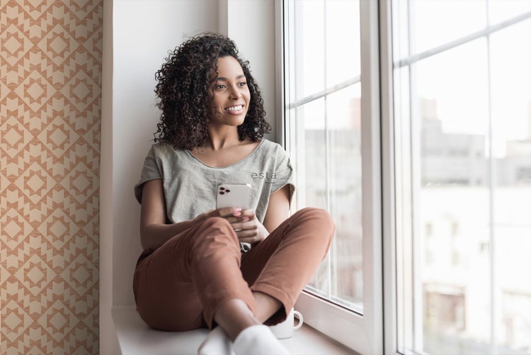 Frau sitzt am Fenster mit gemusterter Tapete