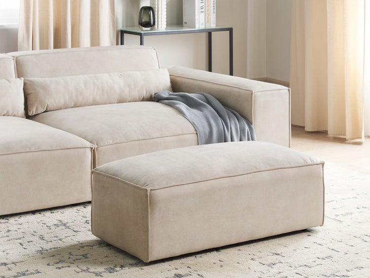 Großer rechteckiger Polsterhocker und passendes Ecksofa in einem modernen, hellen Wohnzimmer auf einem gemusterten Teppich.