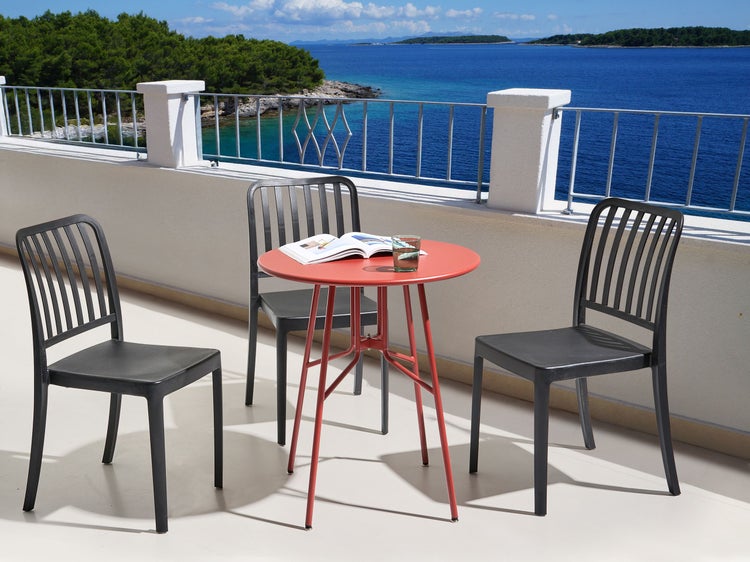 Terrassenszene mit rotem Tisch und schwarzen Stühlen mit Meerblick