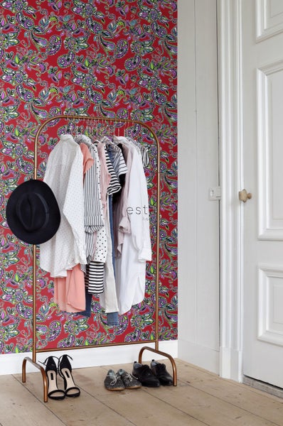 Kleiderständer mit Kleidung vor gemusterter Tapete in einem hellen Raum.