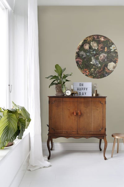 Interieuransicht mit einem Holzschrank, einer Zimmerpflanze und einer runden Wanddekoration mit Blumenmuster
