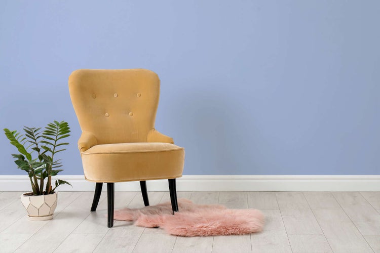 Gelber Samtsessel mit Knopfsteppung auf hellem Laminatboden neben einer Zimmerpflanze und einem Kunstfellteppich.