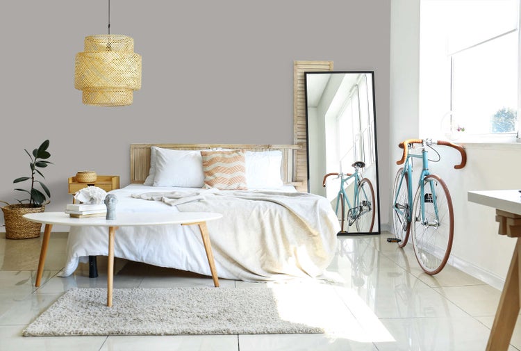 Hell eingerichtetes Schlafzimmer mit grauer Wand, Holzbett, weißer Bettwäsche, Bambus-Pendelleuchte, Standspiegel und einem blauen Rennrad.